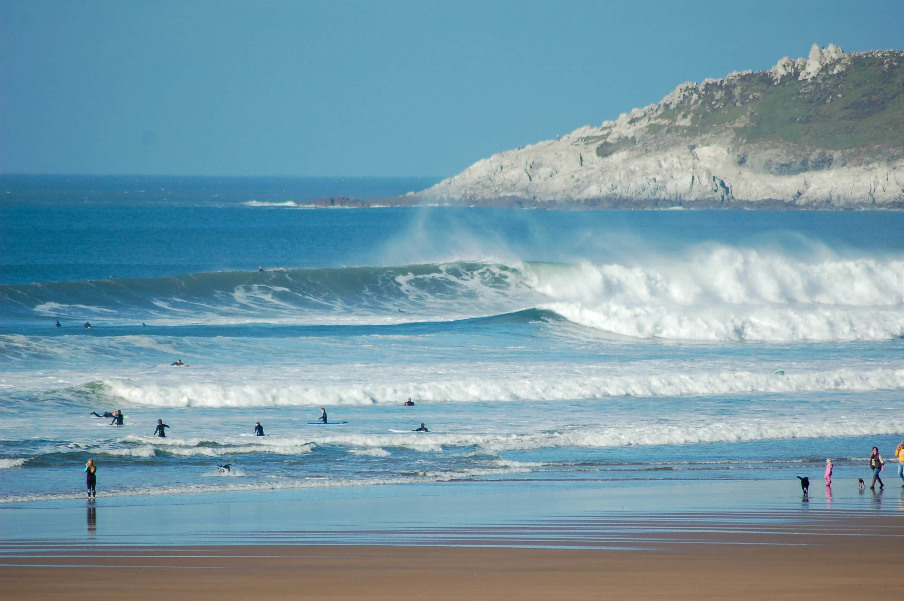 A beach with waves, a cliff, and people.