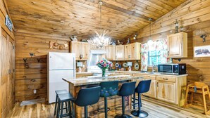 A wooden cabin interior with a kitchen, bar stools, and a refrigerator. - Great for Elk Viewing! Creekside Maggie Valley Gem (Maggie Valley)