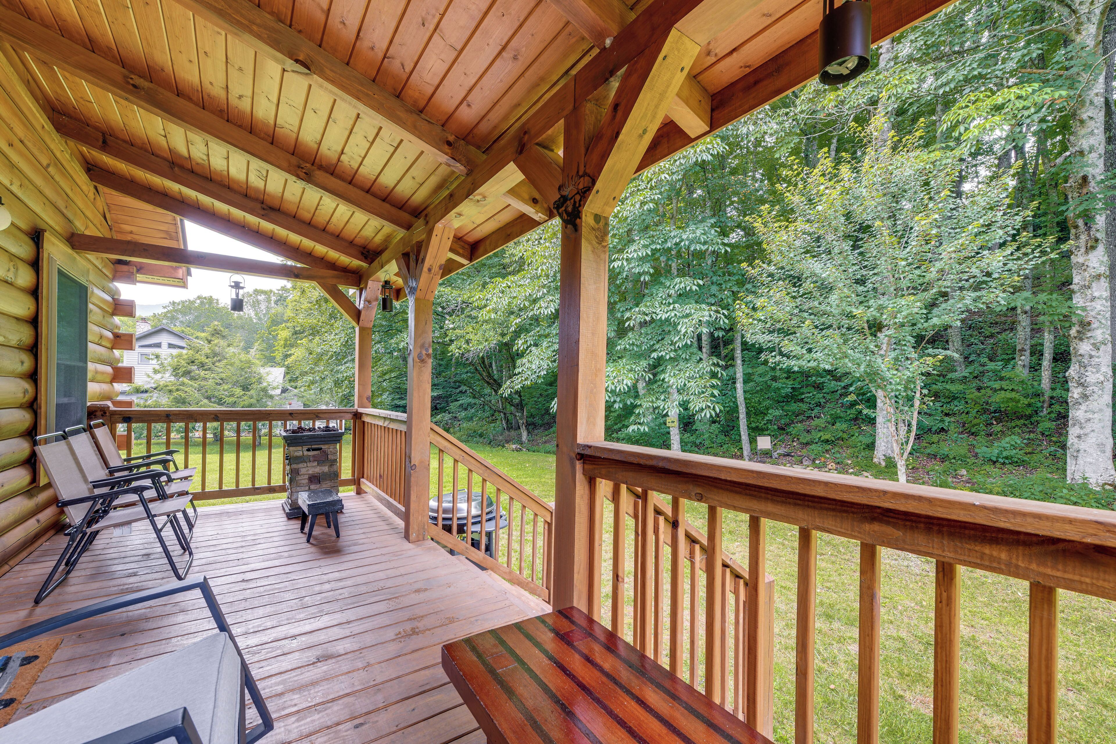 A wooden deck with a view of a forest, a barbecue grill, and a table with chairs.