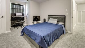 Quarto com cama, escrivaninha com teclado, televisão e janela com cortinas.