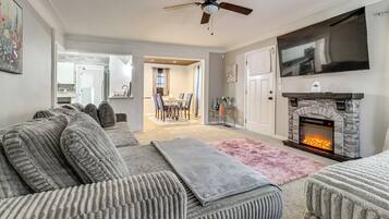 A living room with a fireplace, a ceiling fan, and a TV mounted on the wall.