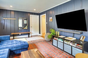 A living room with a sectional sofa, a flat-screen TV, a bookshelf, and a patterned rug. - 2 Mi to UNC Campus! Quiet Escape w/ Deck & Grill (Carrboro)