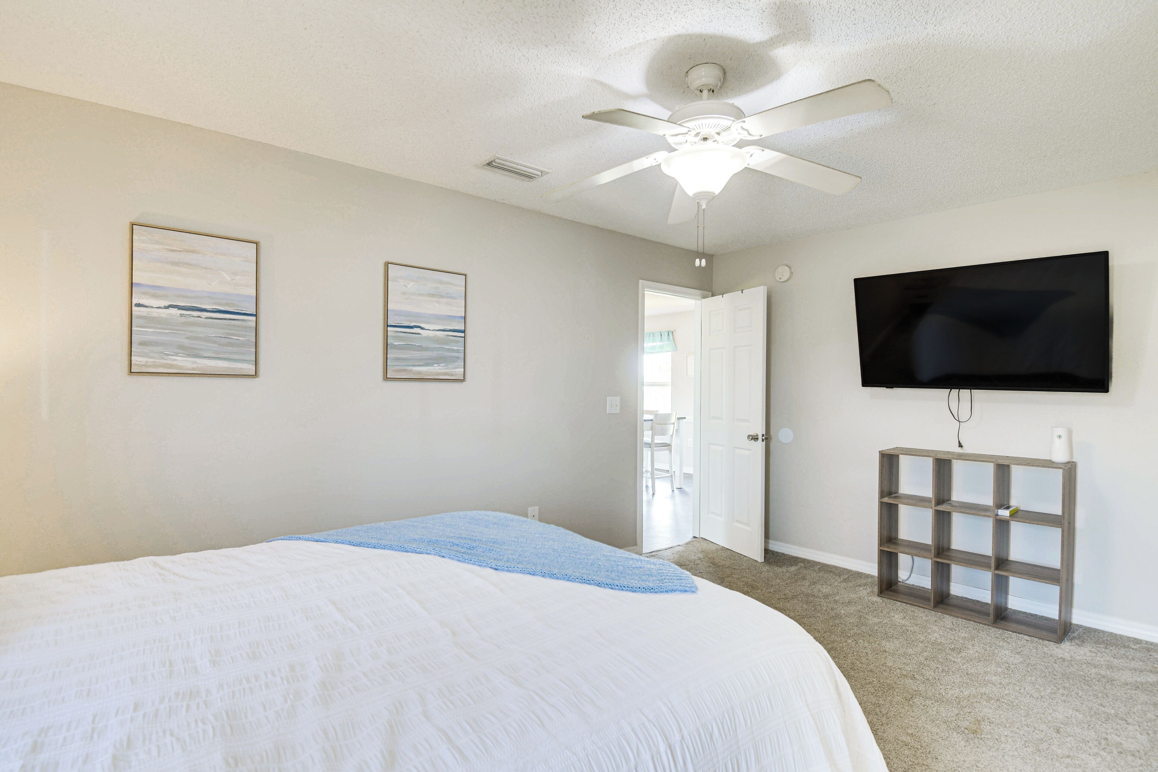 A bedroom with a bed, ceiling fan, artwork, TV, and a door leading to a balcony.