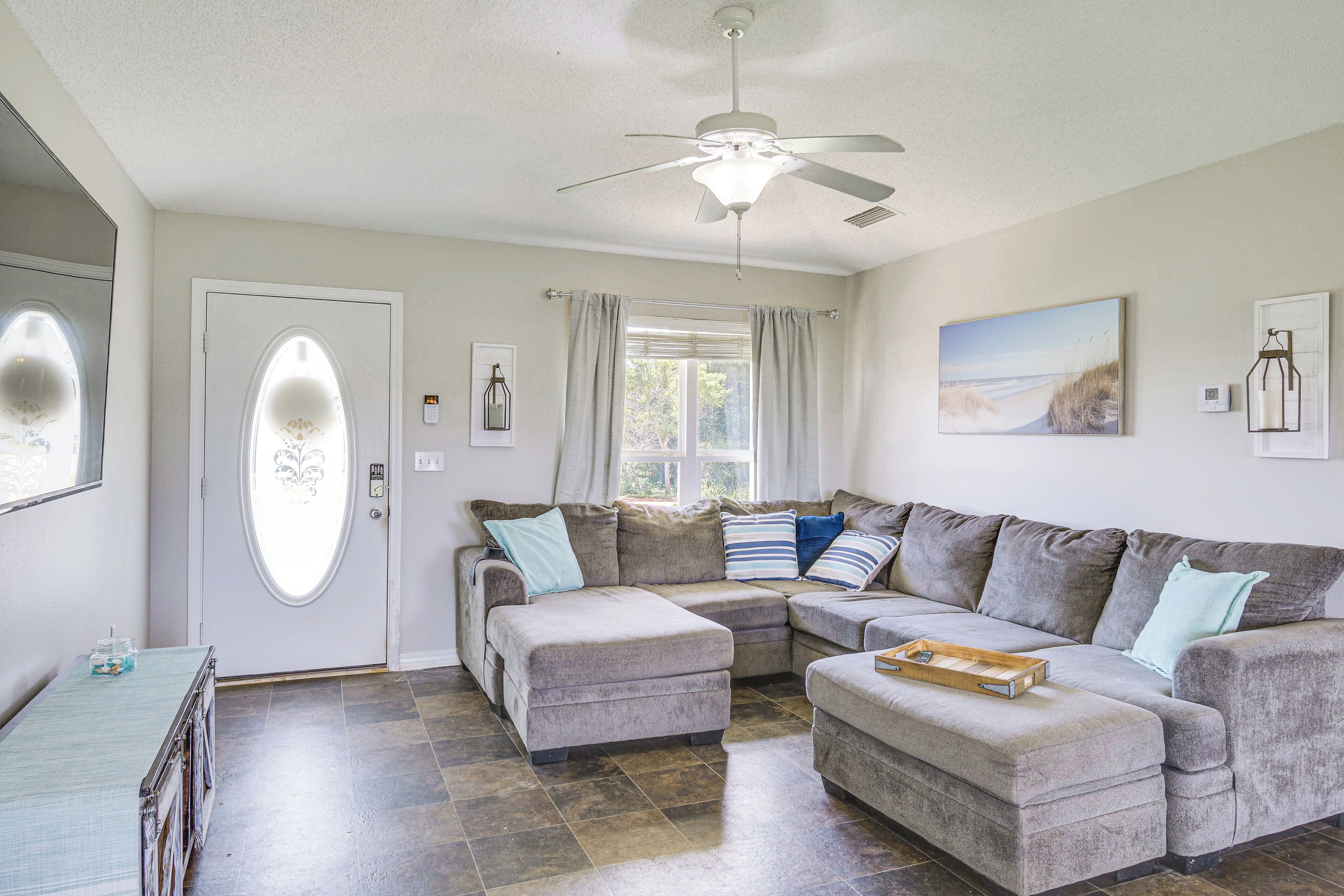 A living room with a sectional sofa, ottoman, ceiling fan, and a window with curtains.