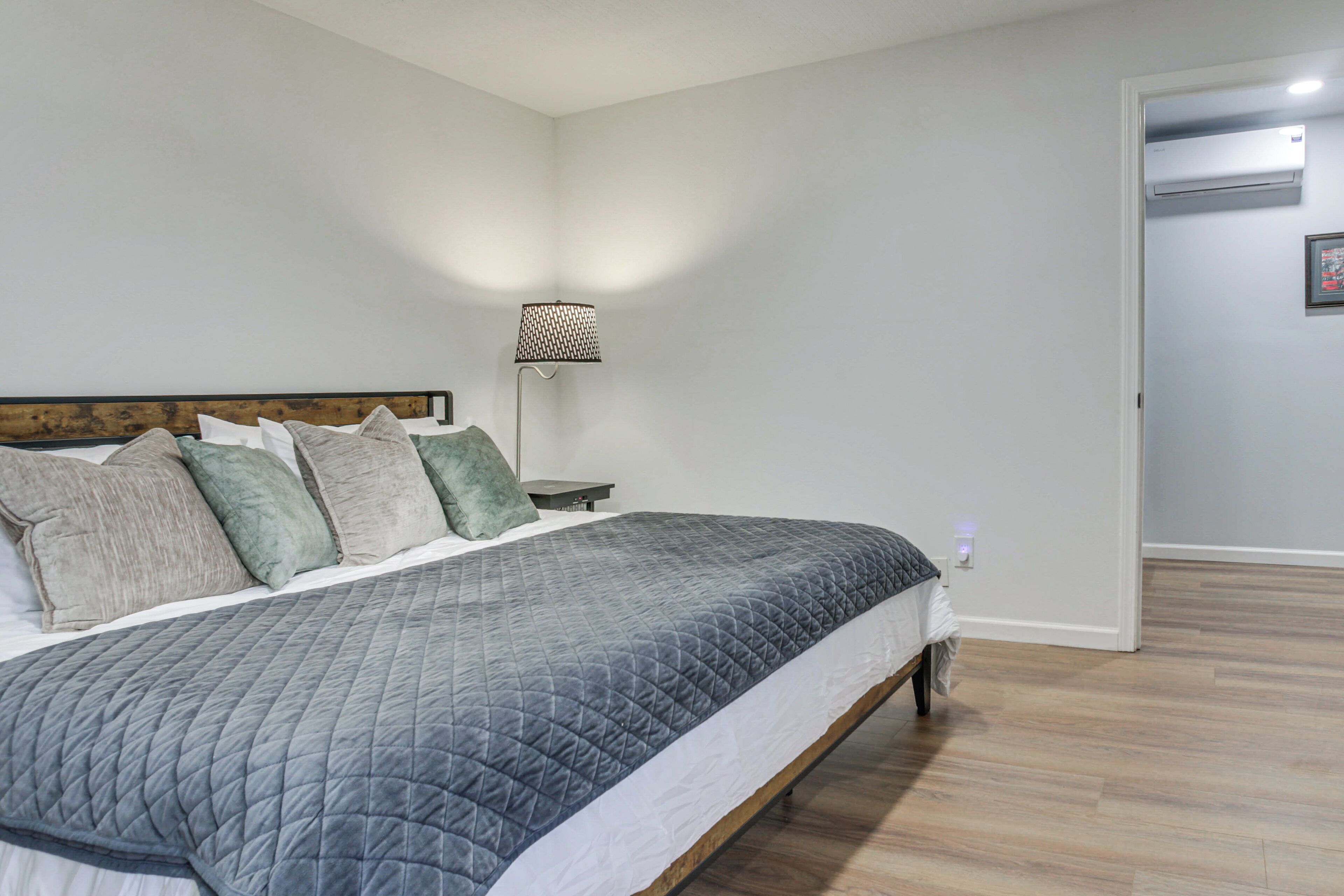 A bedroom with a bed, pillows, a nightstand, a lamp, and an air conditioning unit.