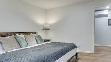 A bedroom with a bed, pillows, a nightstand, a lamp, and an air conditioning unit.