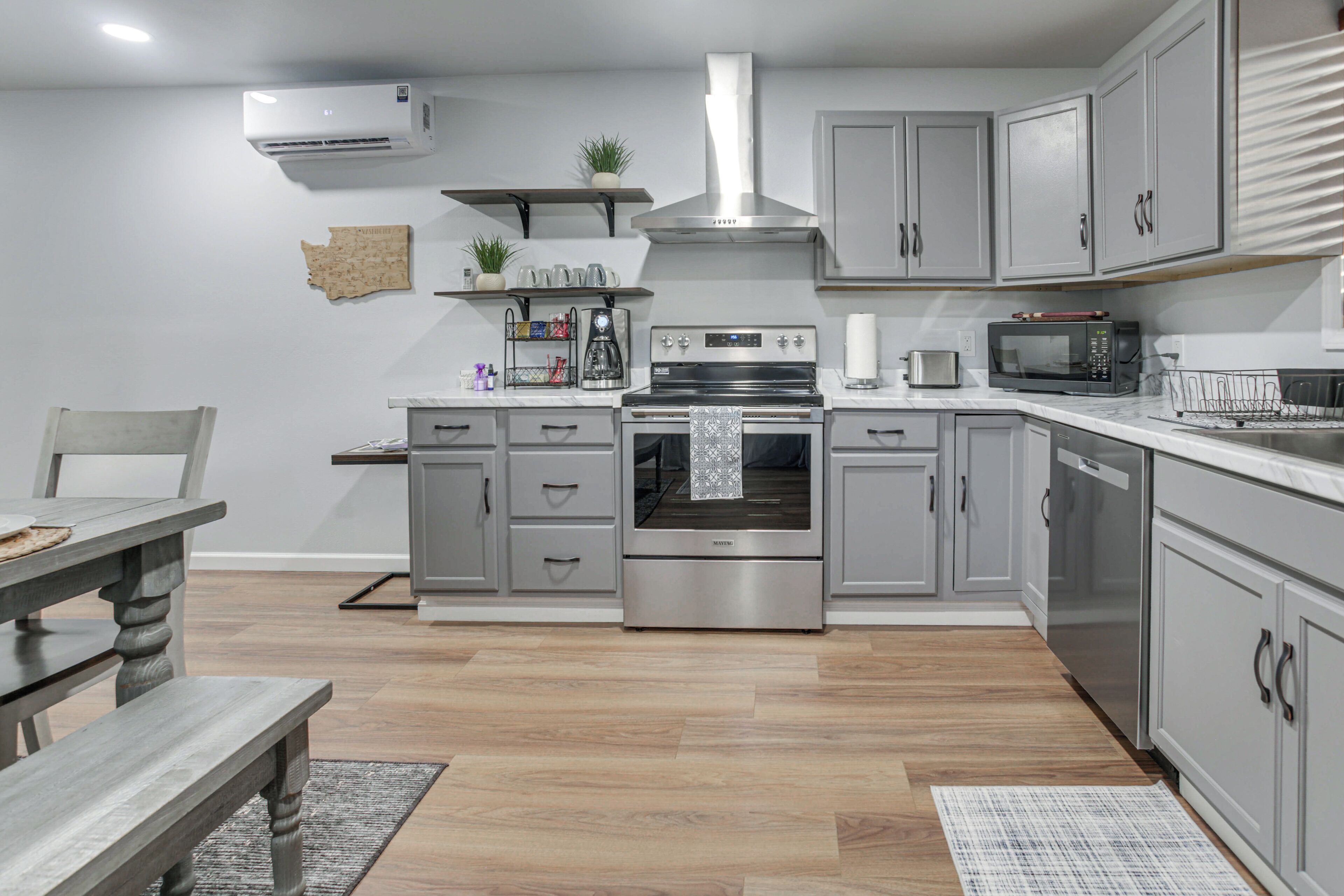 A modern kitchen with grey cabinets, a stainless steel range hood, a built-in oven, a microwave, and a coffee maker.