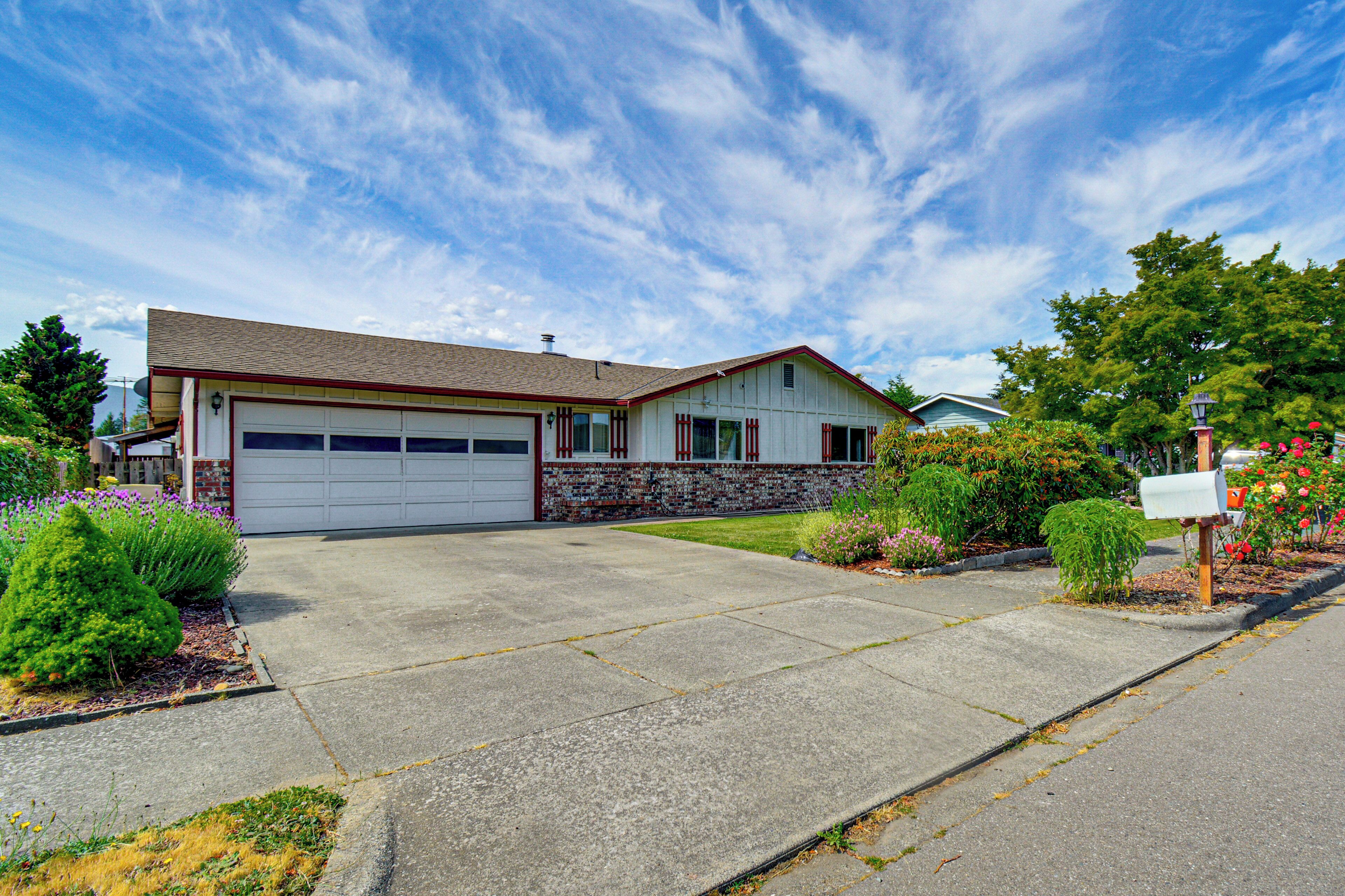 A residential house with a garage, a front yard with plants, and a mailbox.