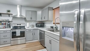 A modern kitchen with stainless steel appliances, grey cabinets, and a wooden floor.