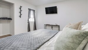A bedroom with a bed, a TV mounted on the wall, a window with curtains, and a coat rack.