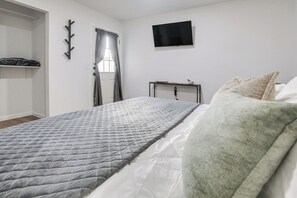 A bedroom with a bed, a TV mounted on the wall, a window with curtains, and a coat rack. - 2-unit Family Combo, Walk to Downtown Sequim! (Sequim)