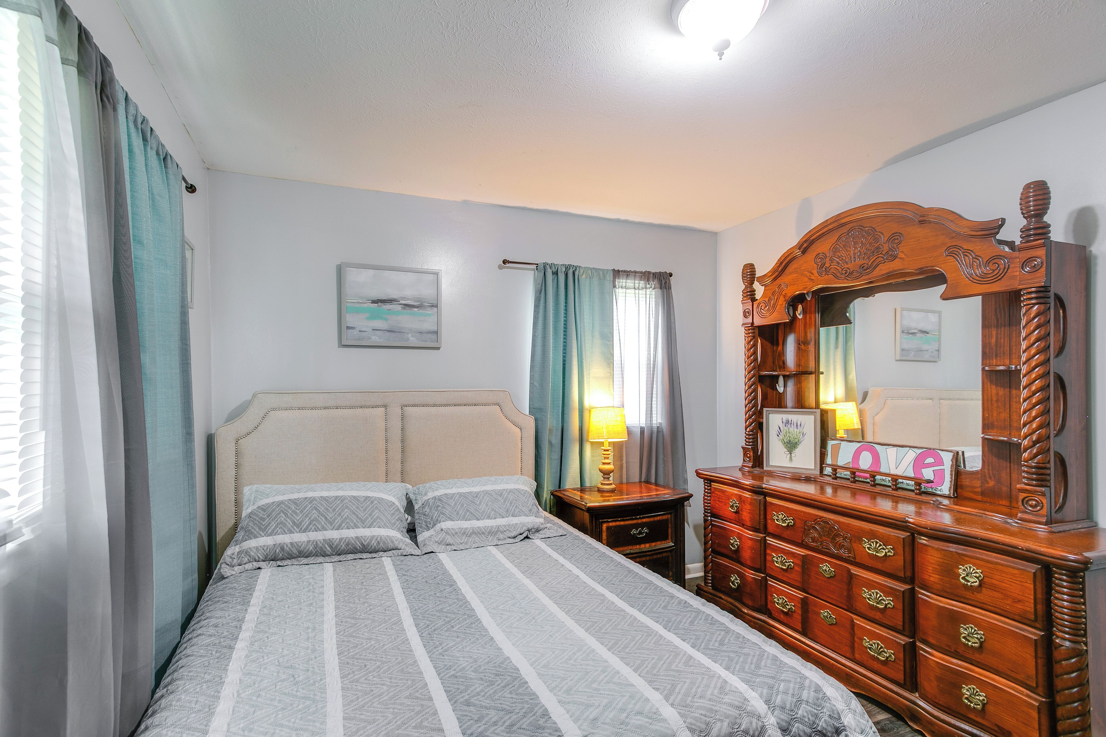 A bedroom with a bed, a dresser, a nightstand, a lamp, and a mirror.