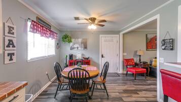 A dining area with a round table, four chairs, a ceiling fan, and a window with blinds.