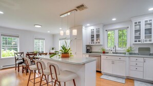 A modern kitchen with white cabinetry, a central island with bar stools, and pendant lighting. - Serene & Sleek Family Retreat w/ Office in Shirley (Shirley)