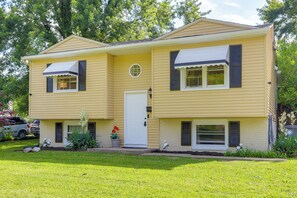 Une maison jaune à deux étages, avec une porte blanche, deux fenêtres dotées de volets et un petit porche.