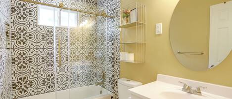 A bathroom with patterned tiles, a bathtub, a toilet, a sink, and a mirror.