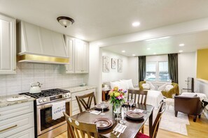 A modern kitchen with a stove, oven, and white cabinets. There is a dining area with a table set for two, chairs, and a vase of flowers. - Explore Oberlin! Home 1 Mi to Main Street & Campus (Oberlin)