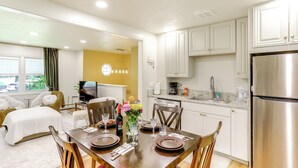 A modern kitchen with white cabinets, a stainless steel refrigerator, and a dining area with a wooden table set for four. - Explore Oberlin! Home 1 Mi to Main Street & Campus (Oberlin)
