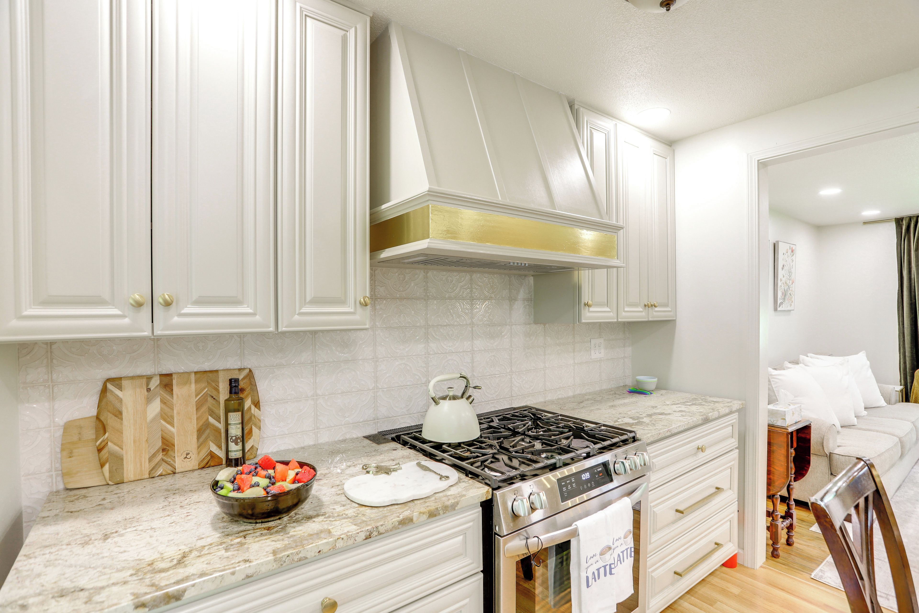 A kitchen with white cabinets, a gas stove, a kettle, and a bowl of fruit.