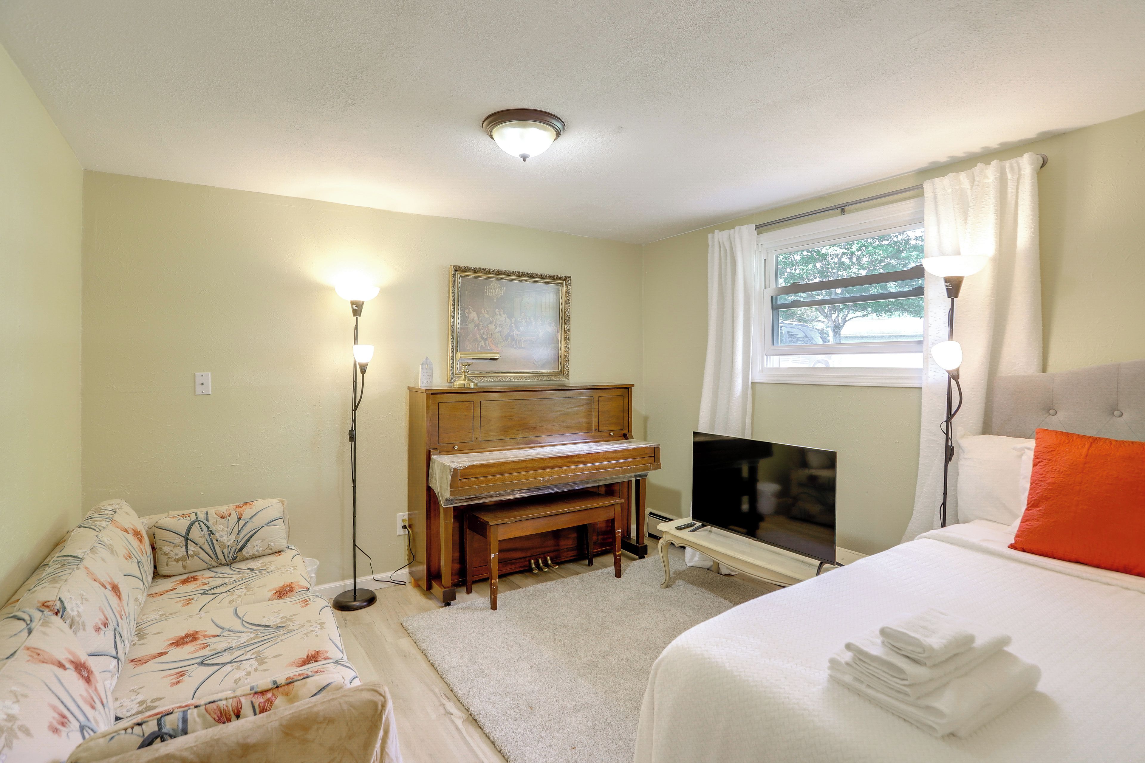 A hotel room with a bed, a sofa, a television, a piano, and a painting on the wall.