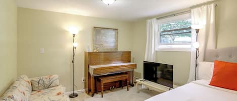 A hotel room with a bed, a sofa, a television, a piano, and a painting on the wall.