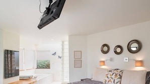 A bedroom with a bed, bedside lamps, a TV, a window, and wall decorations. - Crows Nest TOT #1952 (The Sea Ranch)
