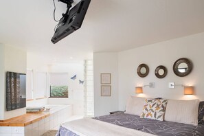 Ein Schlafzimmer mit einem Bett, Nachttischlampen, einem Fernseher, einem Fenster und Wanddekorationen.