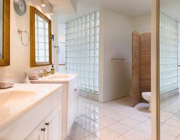A bathroom with two sinks, a mirror, a clock, and a shower area with a glass door. - Crows Nest TOT #1952 (The Sea Ranch)