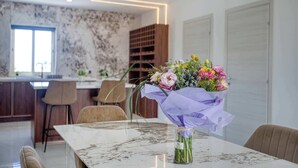 Un espace repas moderne avec une table en marbre, un vase de fleurs et une cuisine en arrière-plan.