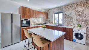 Une cuisine moderne dotée d’un îlot central, de meubles en bois, d’appareils électroménagers en acier inoxydable et d’un dosseret en marbre.