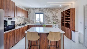 Une cuisine moderne avec des meubles en bois, un îlot central doté de tabourets de bar, un meuble à vin intégré et une grande fenêtre.