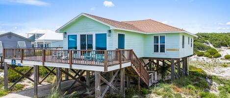 A beachfront house with a wooden deck and a staircase leading to the main entrance.