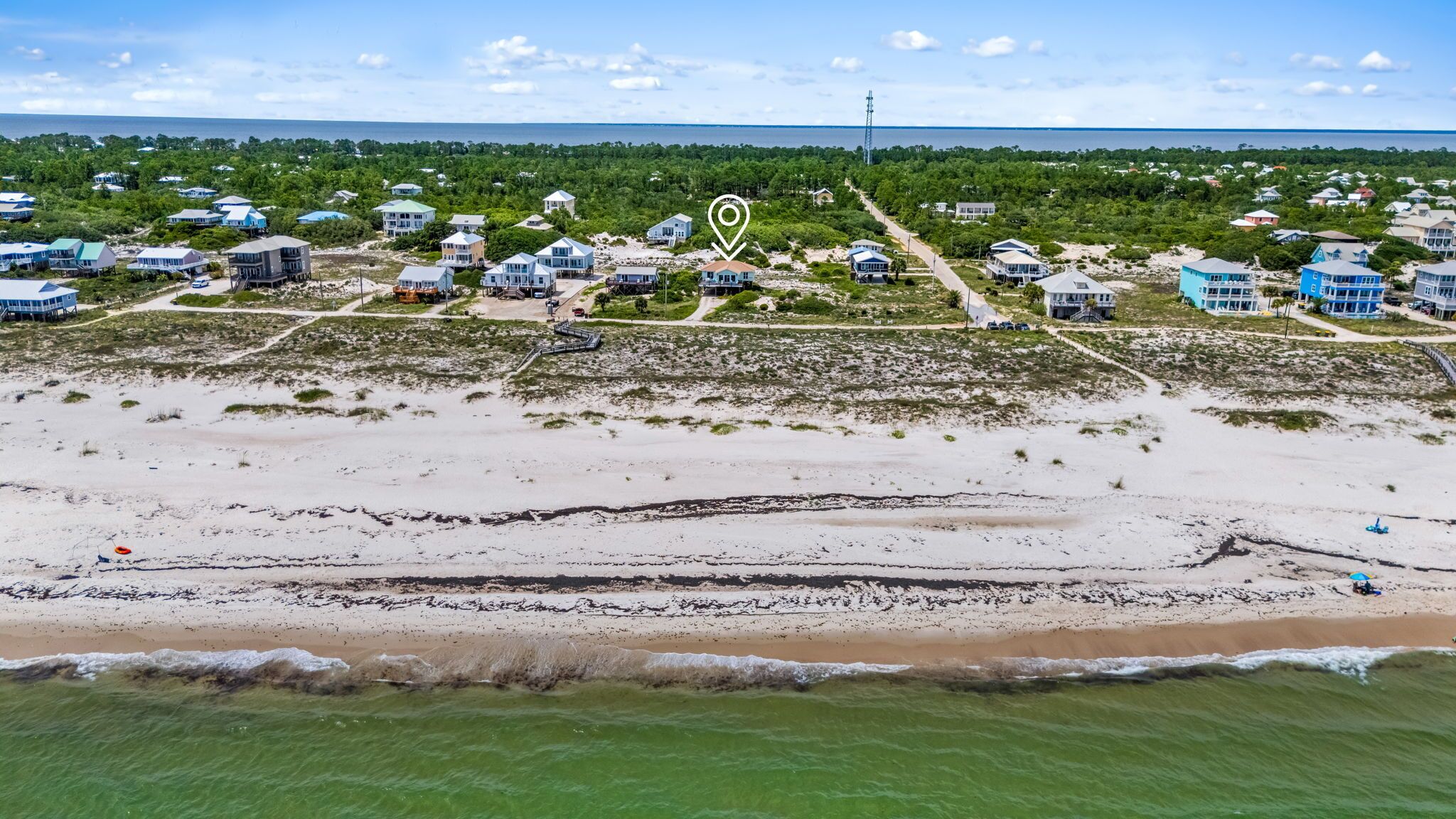 An aerial view of a coastal residential area with houses, a beach, and a clear sky.