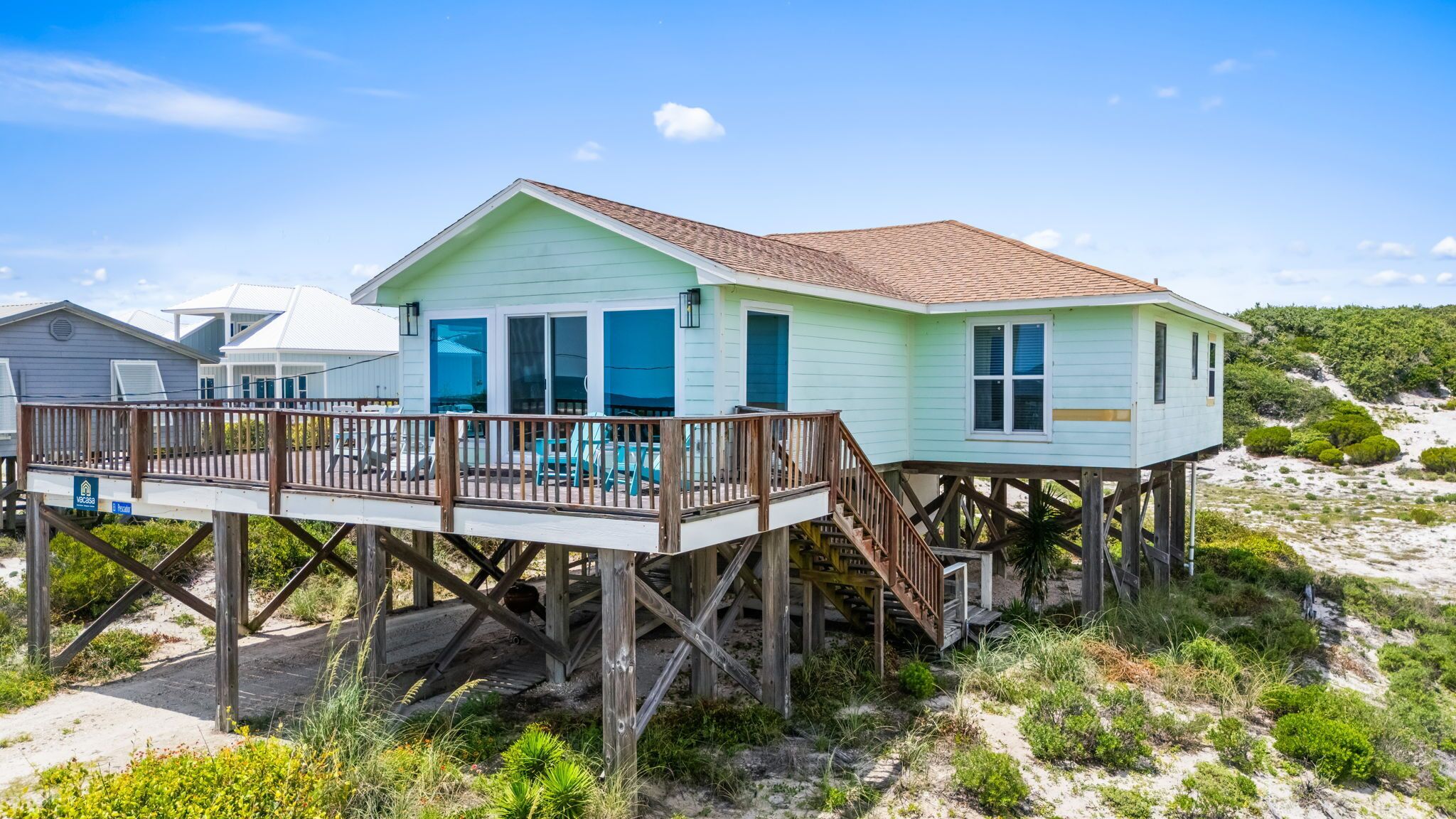 Una casa frente al mar con una terraza de madera y una escalera que conduce a la entrada principal.