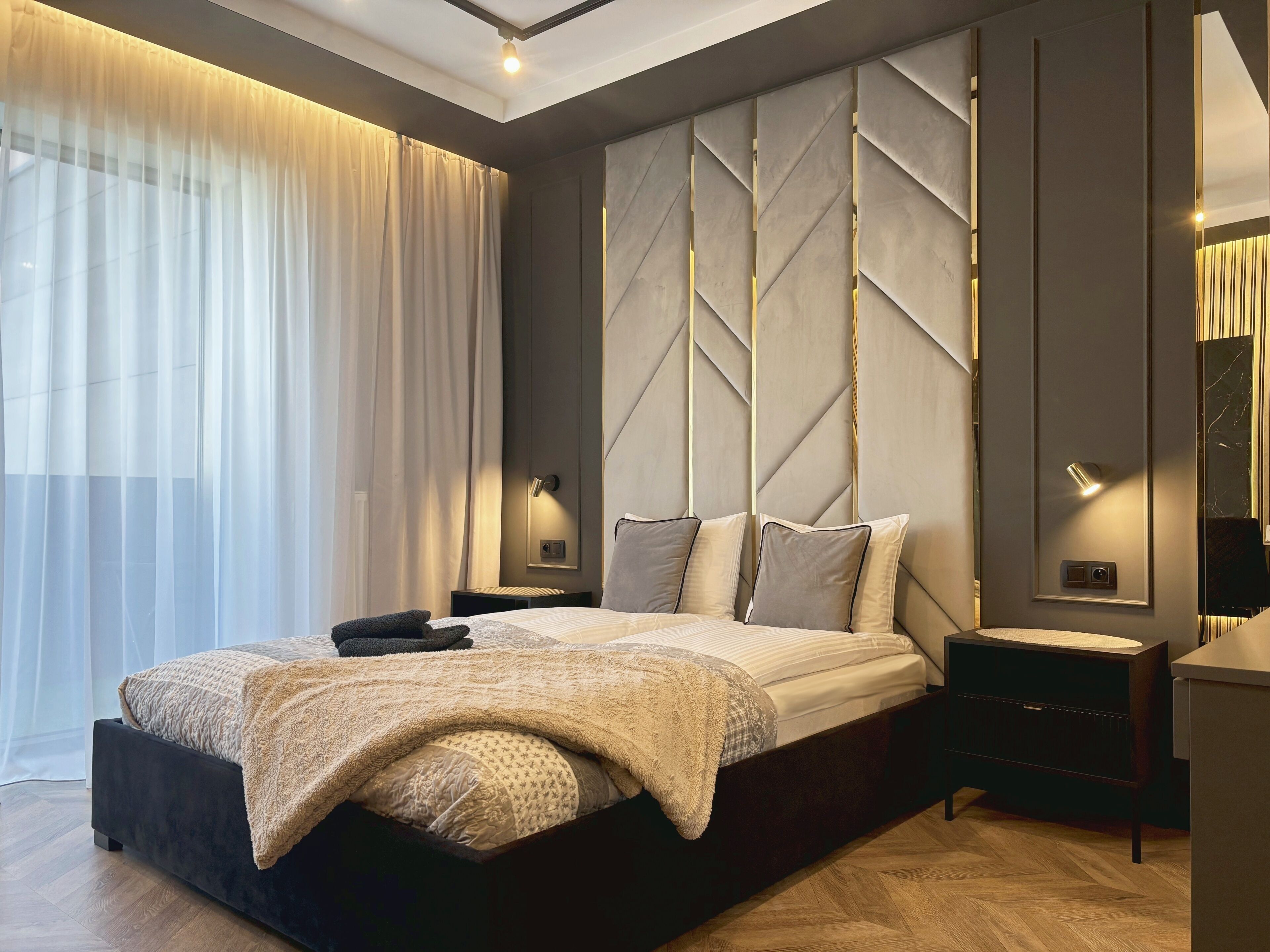 A modern bedroom with a large bed, bedside tables, a mirror, and a view of the outdoors.