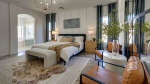 Een moderne slaapkamer met een groot bed, nachtkastjes, een zithoek met een salontafel, en een groot raam met gordijnen.