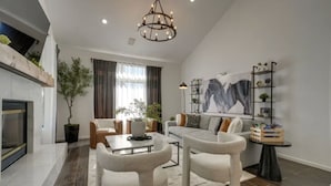 Een moderne woonkamer met een open haard, een kroonluchter, een bank, een salontafel en een boekenkast.