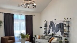 Een moderne woonkamer met een bank, fauteuils, een salontafel, een kroonluchter, een groot schilderij en een boekenkast.