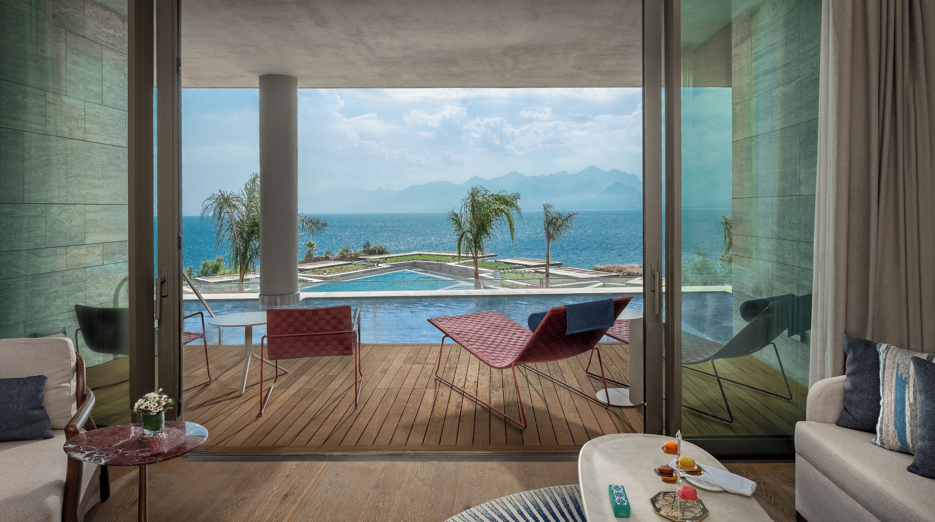 A balcony with a view of a pool and the sea, furnished with chairs and a table.