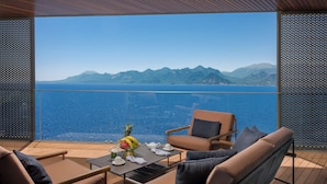 A balcony with a table set for two, a chair, and a view of the sea and mountains. - Divan Talya (Antalya)