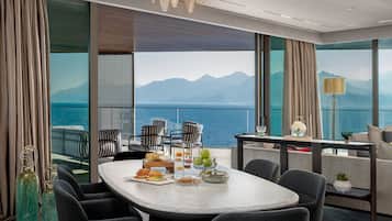 Un espace repas moderne offrant une vue sur la mer et les montagnes, avec une table ronde, des chaises à rayures et une variété de plats et de boissons.