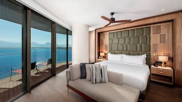 Una habitación de hotel con una cama grande, un balcón con vistas al mar y un ventilador de techo.