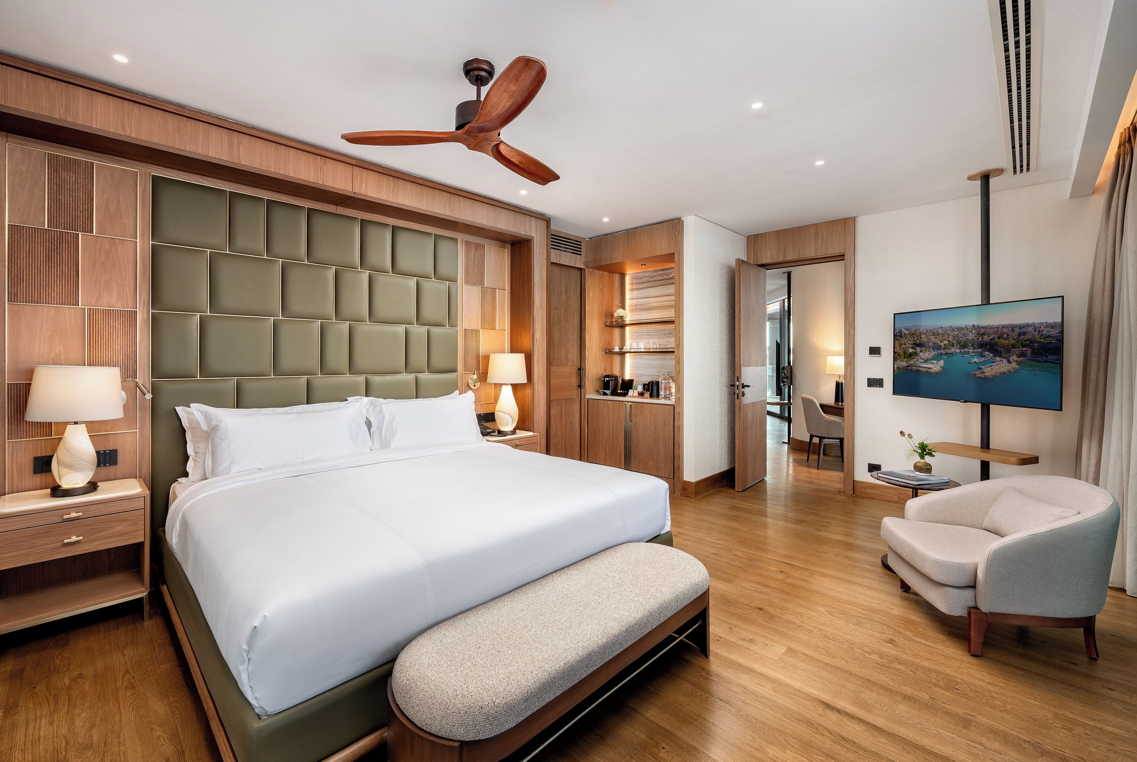 Habitación de hotel con una cama grande, ventilador de techo, televisor y zona de estar.