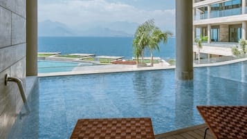 Zona de piscina con vista al mar y montañas, una palmera y una estructura de edificio moderna.
