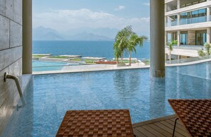 A pool area with a view of the sea and mountains, a palm tree, and a modern building structure. - Divan Talya (Antalya)
