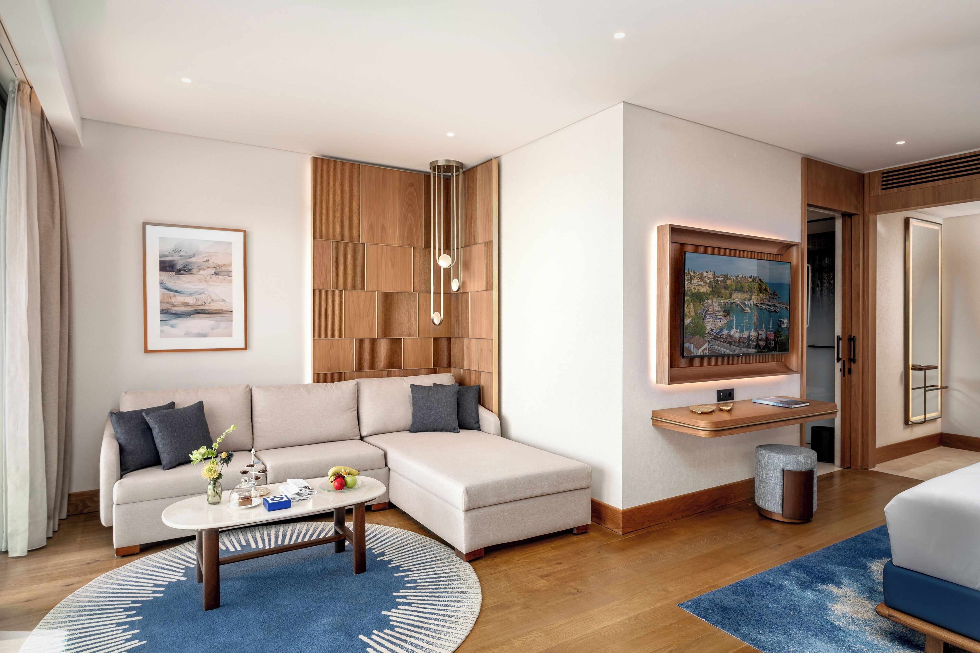 A modern hotel room with a sofa, a coffee table, a TV, and a large window.