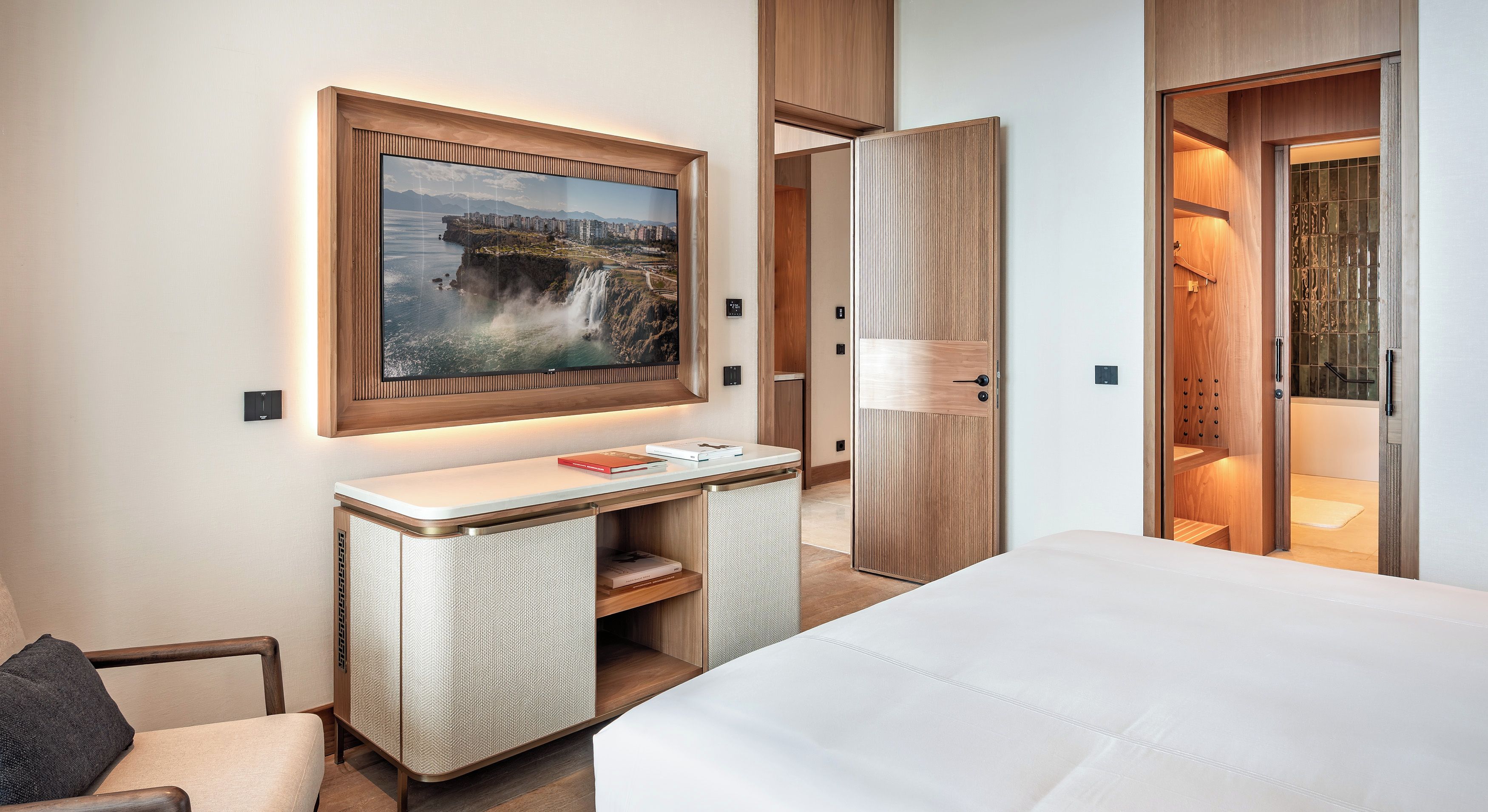 Een hotelkamer met een bed, een bureau met een flatscreen televisie, een kledingkast en een badkamer zichtbaar door een geopende deur.