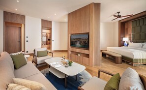 A modern hotel room with a flat-screen TV, a bed, a sofa, a chair, and a small table with a vase and a bowl. - Divan Talya (Antalya)