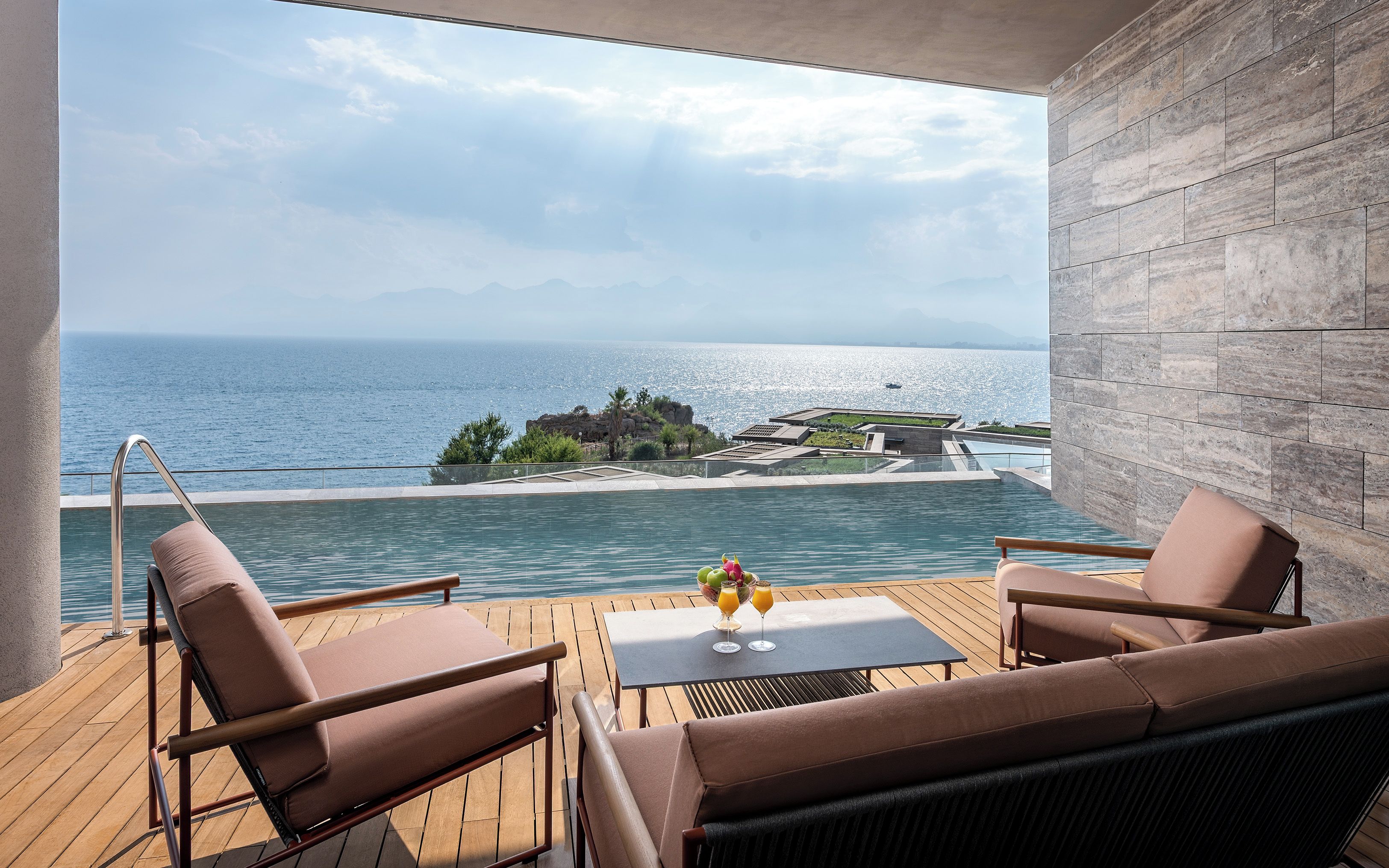 A balcony with a view of the sea, a pool, and a table with drinks.