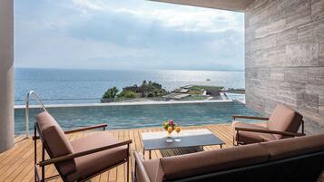 A balcony with a view of the sea, a pool, and a table with drinks.